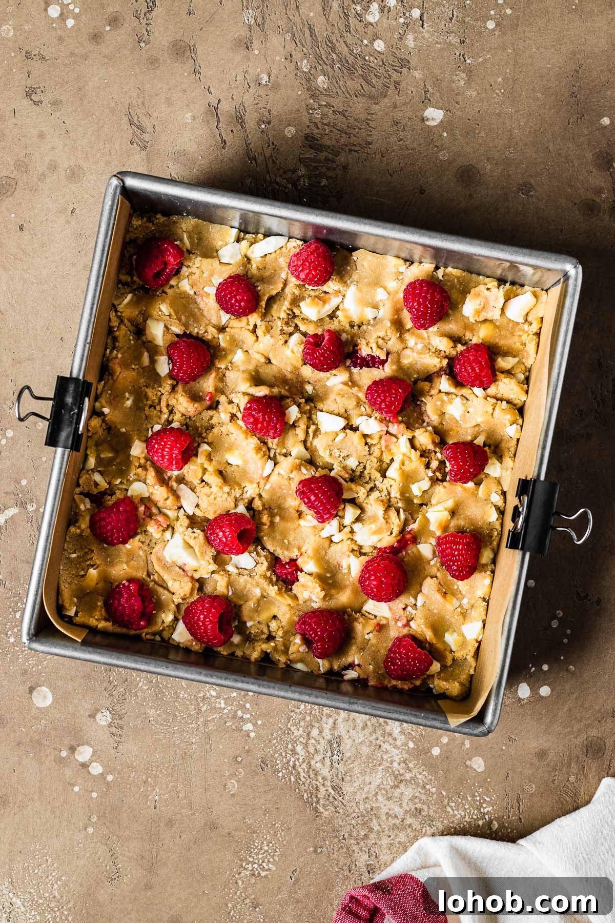 Raspberry White Chocolate Blondies Recipe — Chewy, Fruity Bars 8 A square pan with unbaked blondie dough studded with white chocolate and raspberries.