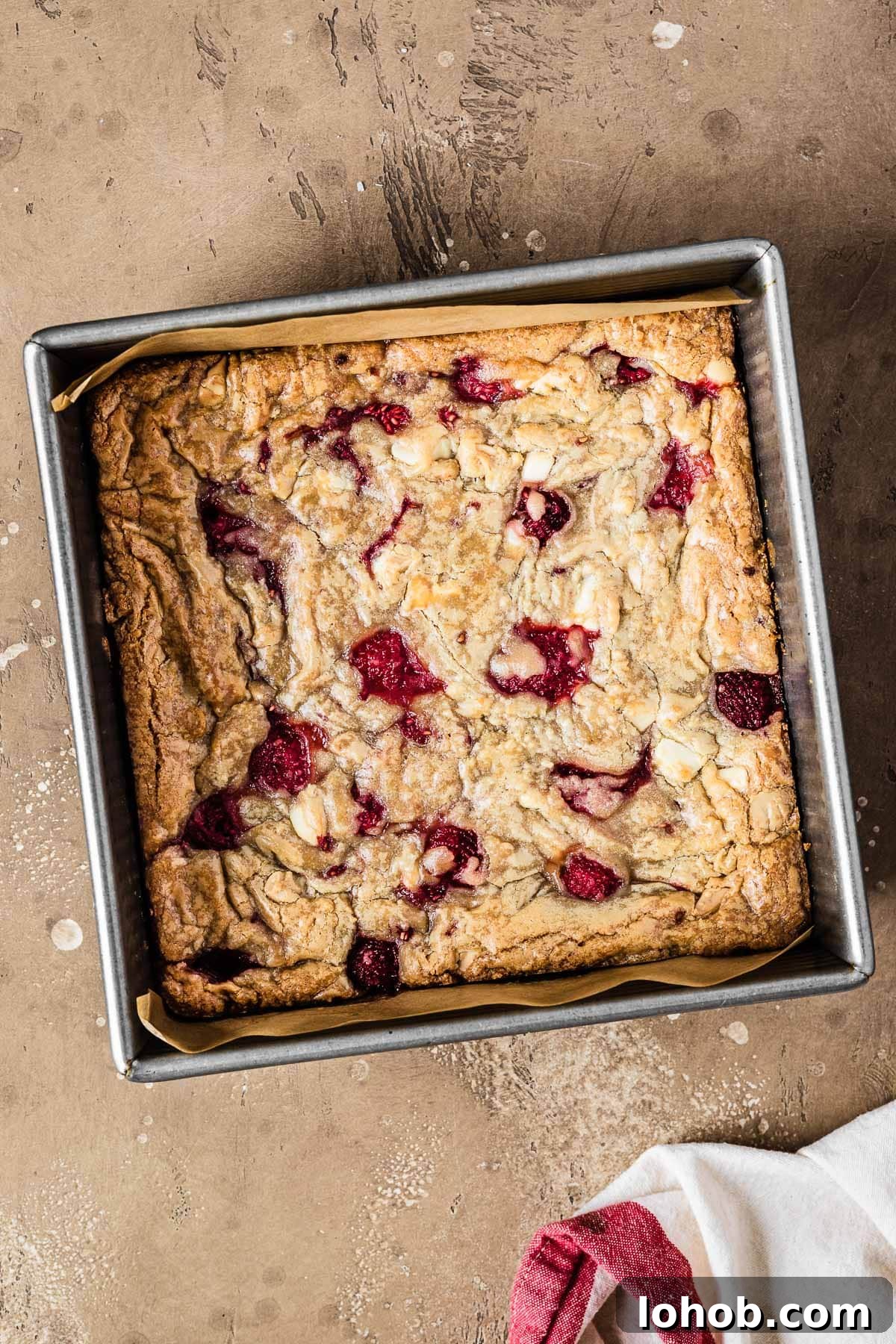 Raspberry White Chocolate Blondies Recipe — Chewy, Fruity Bars 9 A square pan of baked rasberry blondies that have not yet been cut.