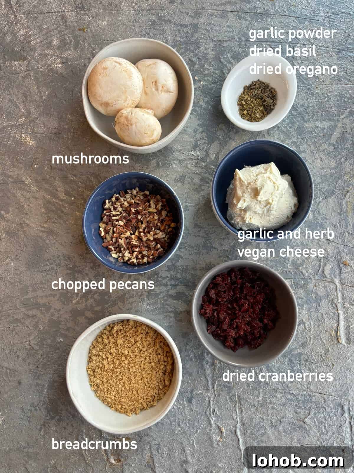 overhead image of the ingredients needed to make vegan stuffed mushrooms. Each ingredient is in it's own small bowl and labeled with white text.