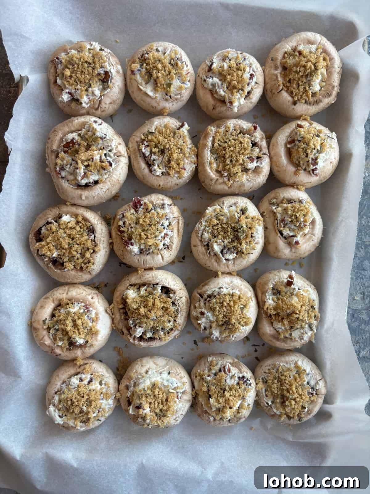 stuffed white button mushrooms topped with breadcrumbs on top of a parchment paper lined baking sheet.