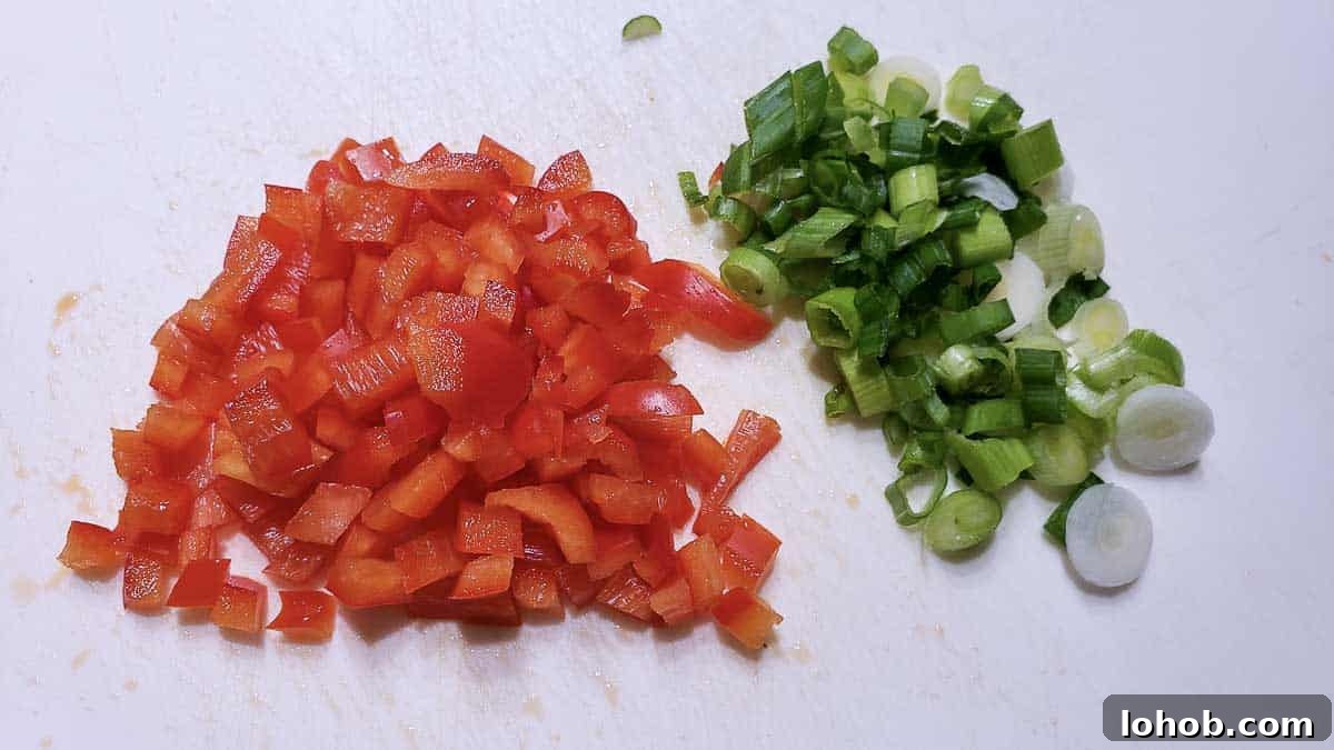 diced green onion and diced red pepper on a cutting board.