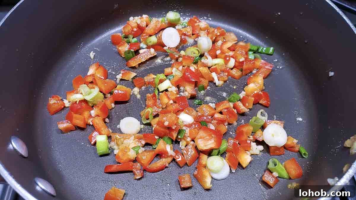 green onion, red pepper, garlic, and ginger cooking in a pan.