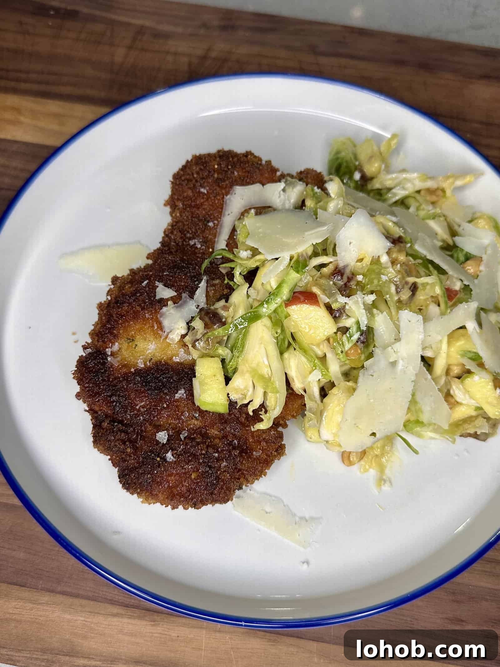 Crispy Chicken Thigh Bites with Shaved Brussels Sprout Salad 2 A white plate with crispy breaded cutlets and a mixed salad topped with shaved cheese, set on a wooden surface.