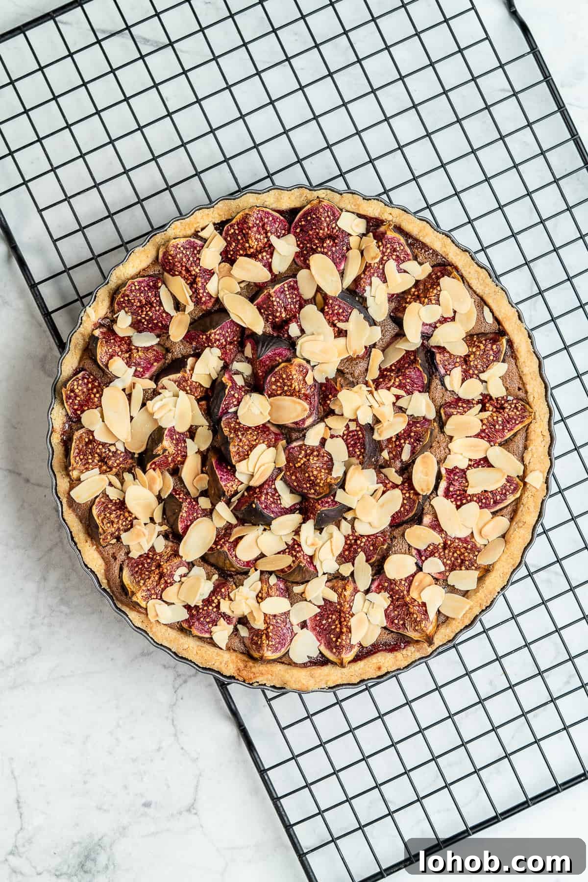 Fig tart with flaked almonds on top on a wire rack.