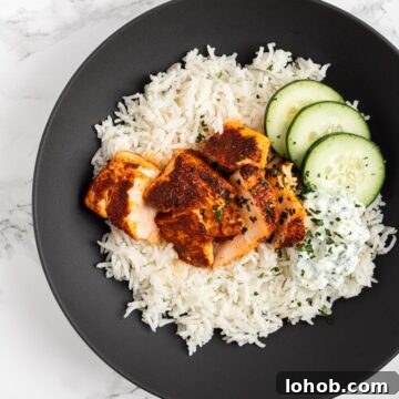 A top down view of a bowl with rice, tandorri salmon, raita and cucumber.