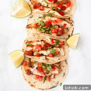 a top down view of a line of grilled chicken tacos surrounded by lime wedges.