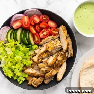 A top down view of a platter with chicken shawarma, lettuce tomato and onion next to pita bread and tahini sauce.