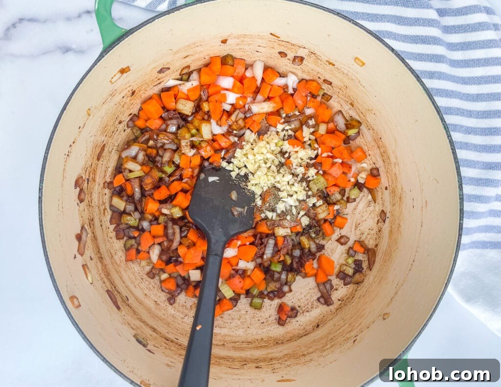 Carrots, garlic, and onions cooking in a pot. A black spatula is stirring.