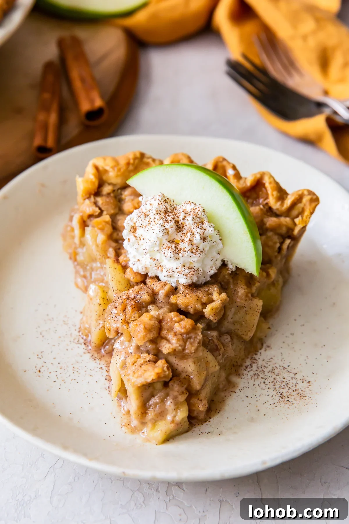 Piece of dutch apple pie with streusel crumb topping, garnished with cream and a green apple slice.