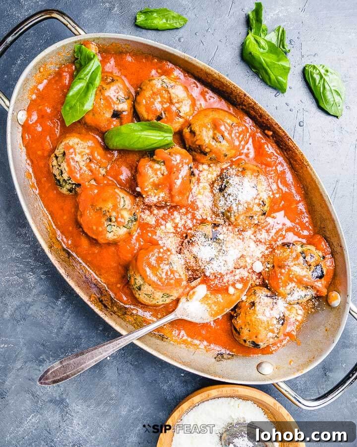 Eggplant meatballs in oval pan with sprinkled basil leaves and bowl of Pecorino Romano cheese.