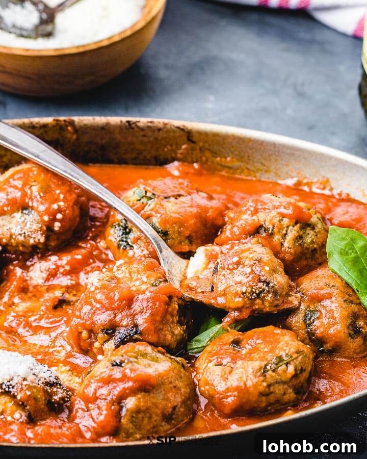 Side angle view of eggplant meatballs in pan with grated Pecorino Romano in background.