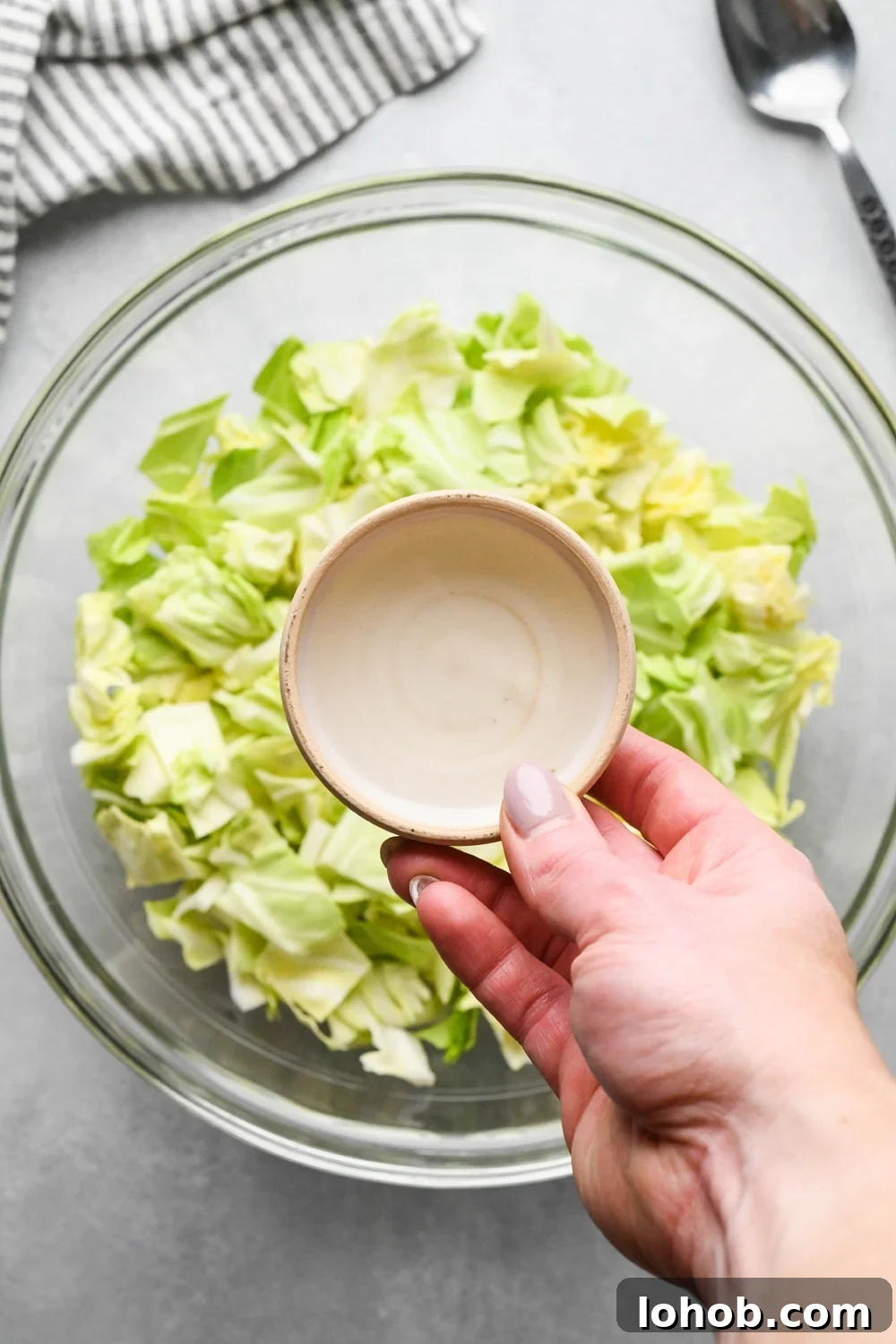 How to make chopped green cabbage salad: A hand adding rice vinegar from a small ceramic dish to the bowl of cabbage. 