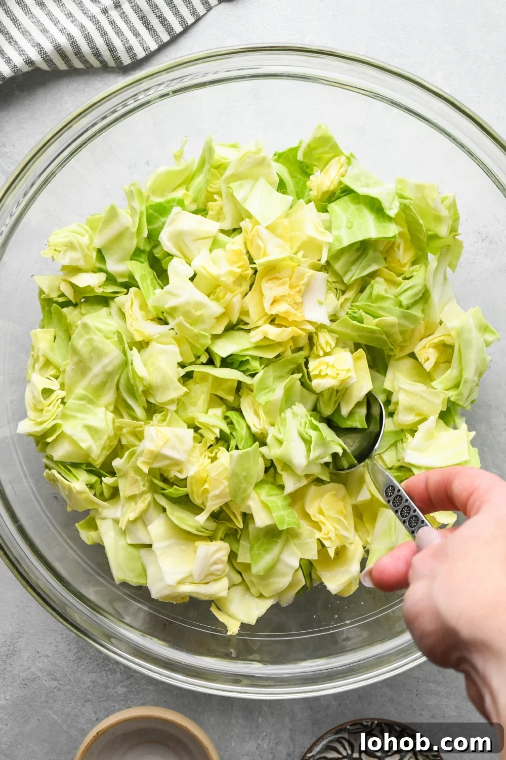 How to make chopped green cabbage salad: Cabbage being tossed together with salt and vinegar using a large metal spoon.