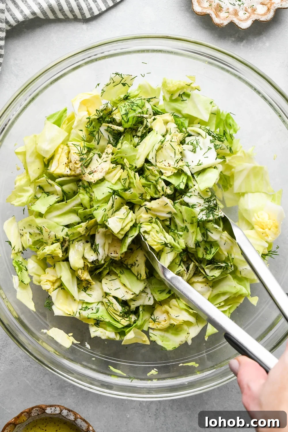 How to make chopped green cabbage salad: Using tongs to toss together the cabbage salad.