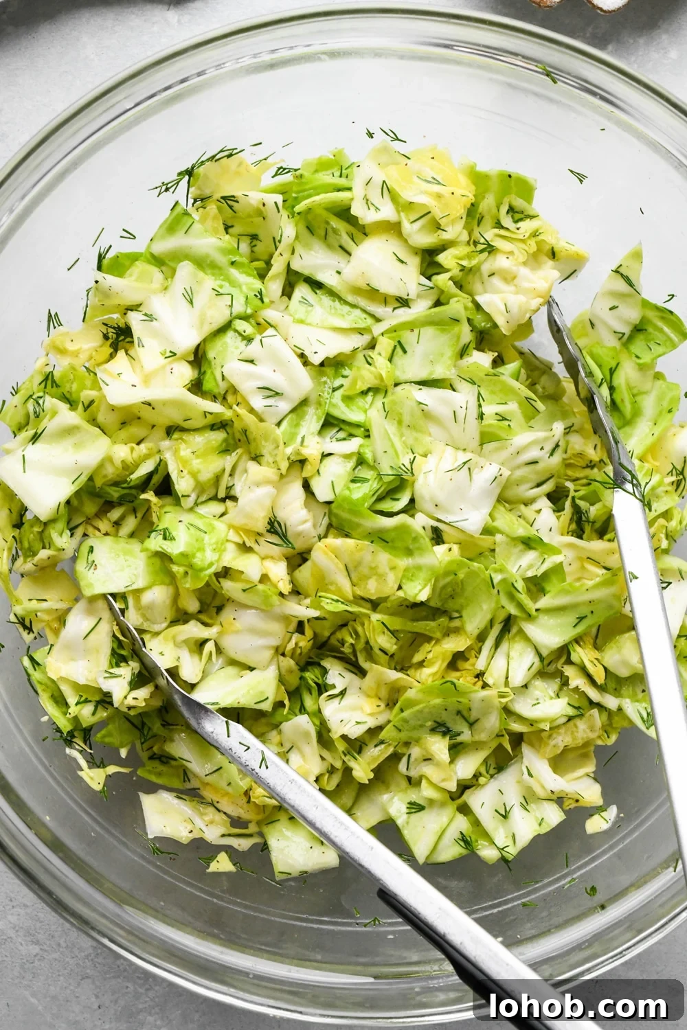 How to make chopped green cabbage salad: Salad after tossing together in a large glass bowl with kitchen tongs angled into the bowl. 