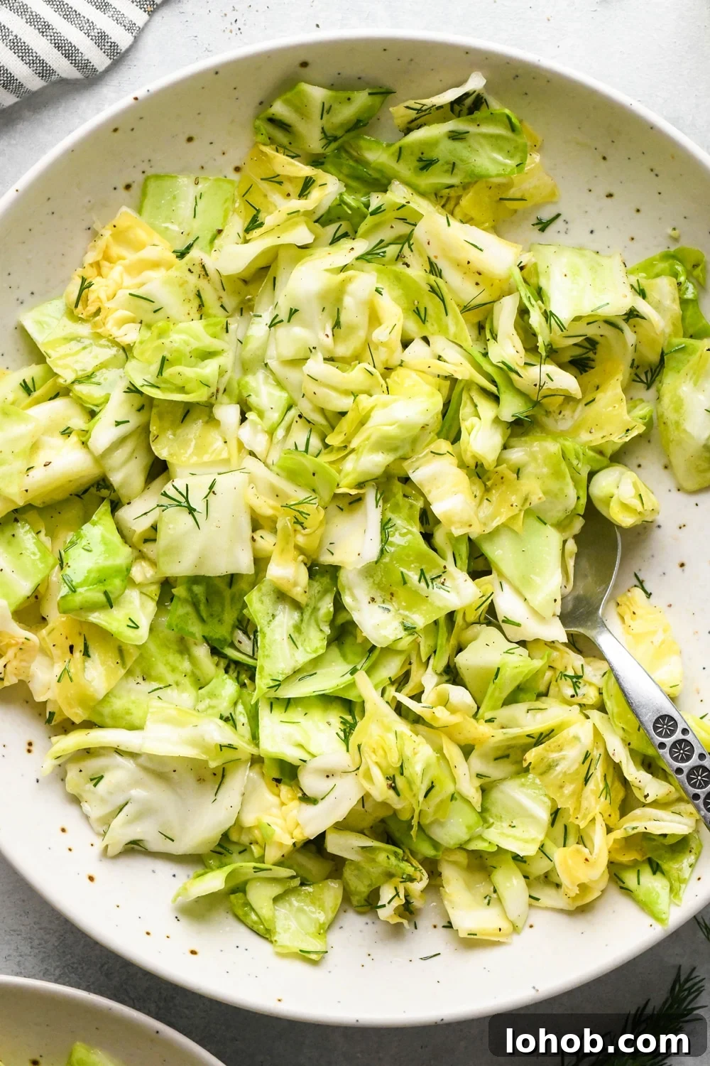 Chopped green cabbage salad with fresh dill in a serving bowl with a portion of the salad scooped out, and a spoon angled into the bowl. 
