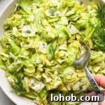 Chopped green cabbage salad with fresh dill in a large shallow serving bowl, garnished with extra sprigs of fresh dill and a spoon is dipping into the salad to lift out a portion for serving.