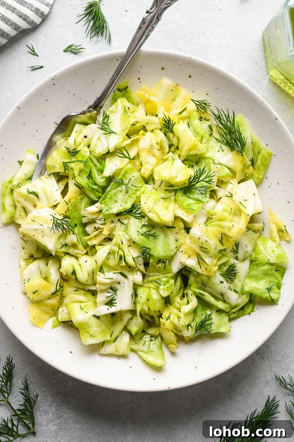 Chopped green cabbage salad in a small salad dish, with a fork angled onto the plate. The salad is garnished with chopped fresh dill.