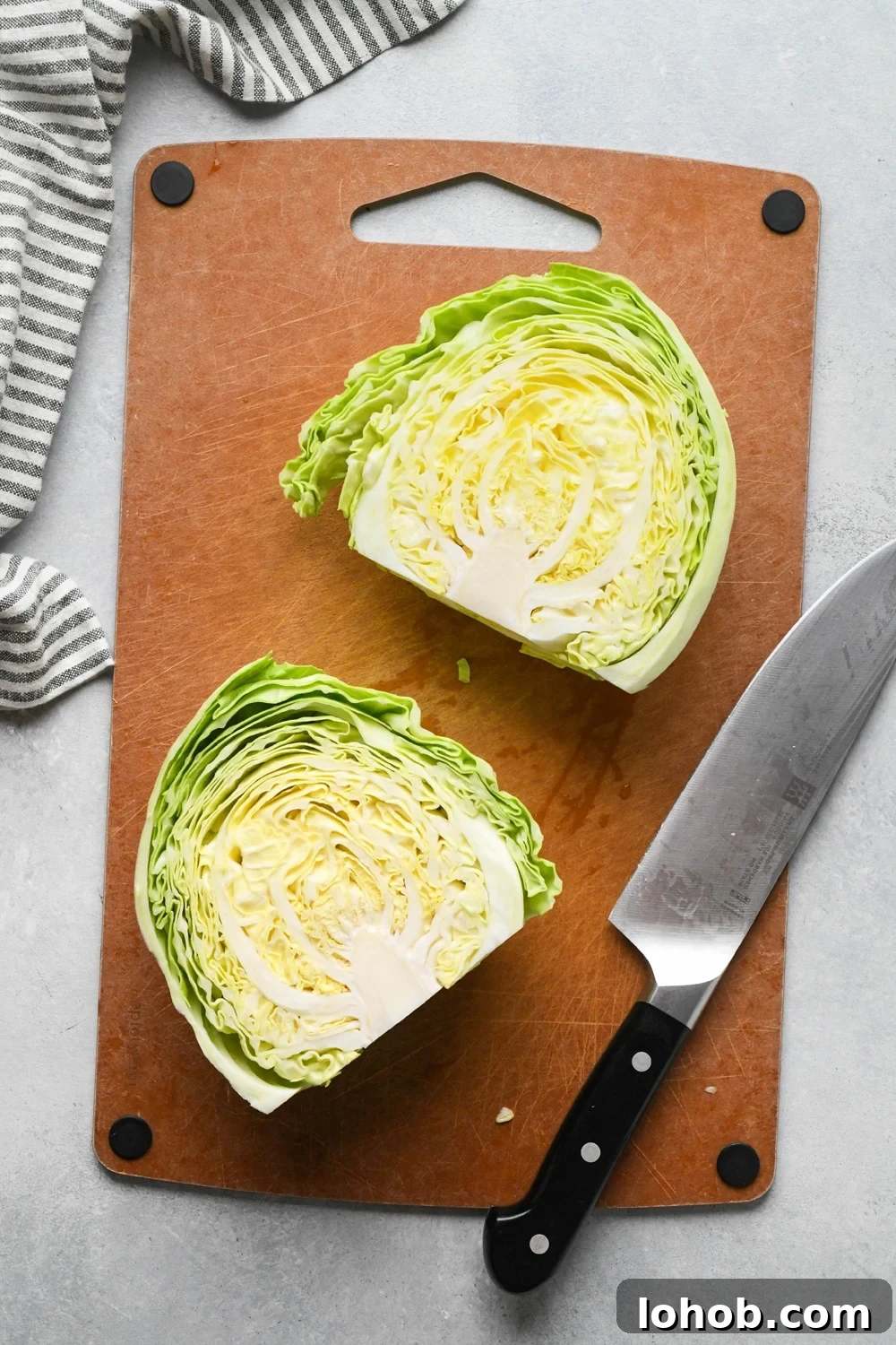 How to make chopped green cabbage salad: Step-by-step showing how to roughly chop cabbage. Small head of green cabbage is cut in half on a cutting board.