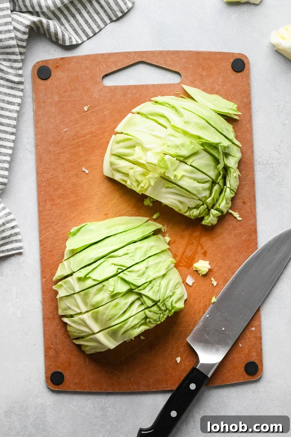 How to make chopped green cabbage salad: Step-by-step showing how to roughly chop cabbage. Small head of green cabbage is cut in half on a cutting board, facing flat side down and cabbage is cut into half inch thick strips.