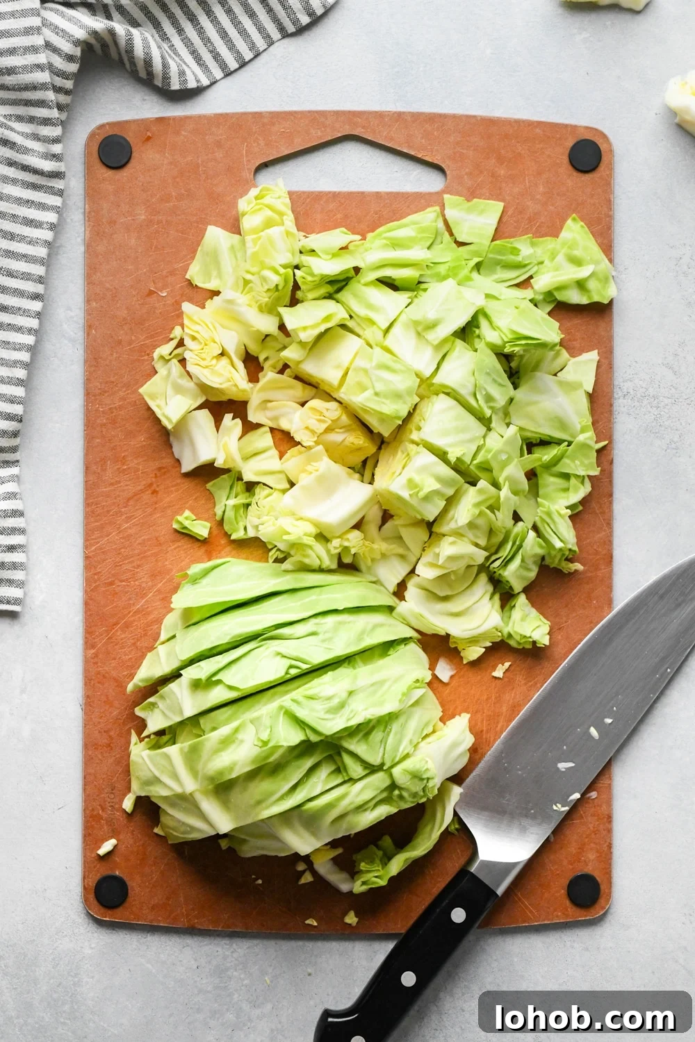 How to make chopped green cabbage salad: Step-by-step showing how to roughly chop cabbage. Small head of green cabbage is cut in half on a cutting board, facing flat side down and cabbage is cut into half inch thick strips. One half of the cabbage has been chopped into bite sized pieces.