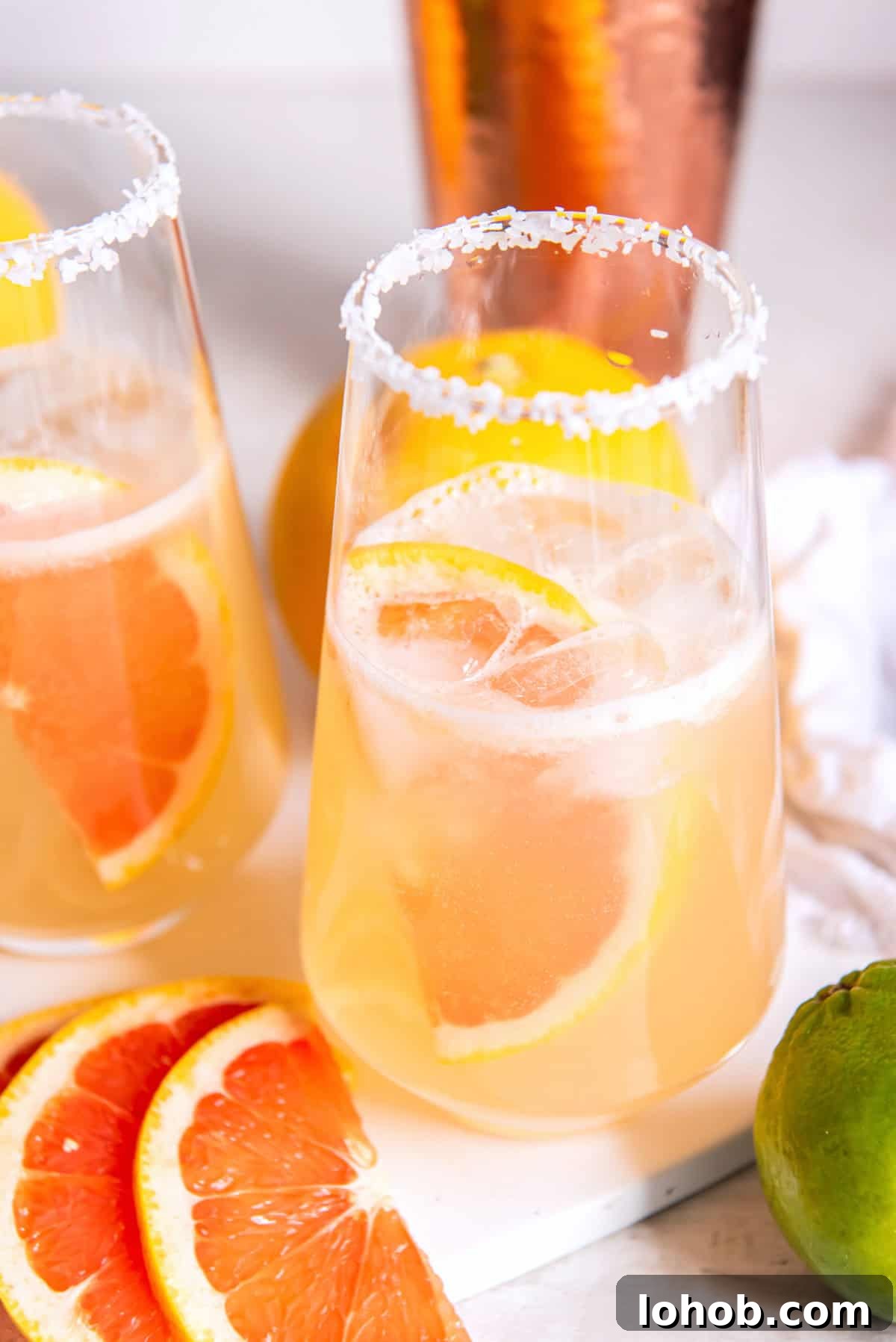 two glasses of pink drinks and a grapefruit wedge floating in the drink.