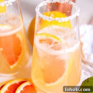two glasses of pink drinks and a grapefruit wedge floating in the drink.