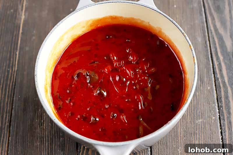 Sweet and Tangy Classic Meatballs Recipe for Weeknight Dinners 11 Horizontal image of a thick, red liquid mixture in a pot.