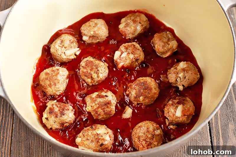 Sweet and Tangy Classic Meatballs Recipe for Weeknight Dinners 12 Horizontal image of browned beef portions in a thick red sauce in a pot.