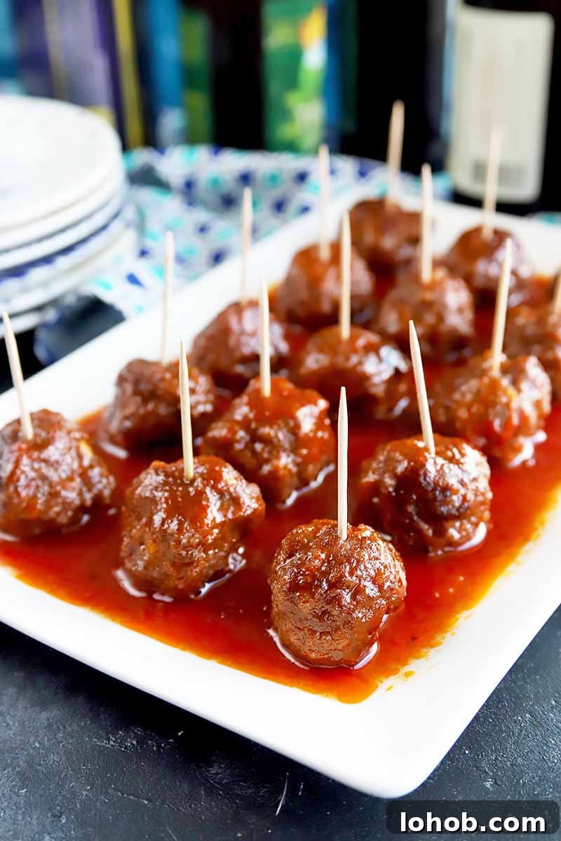 Sweet and Tangy Classic Meatballs Recipe for Weeknight Dinners 3 Vertical image of a white platter with neat rows of meatballs with toothpicks covered in a red sauce.