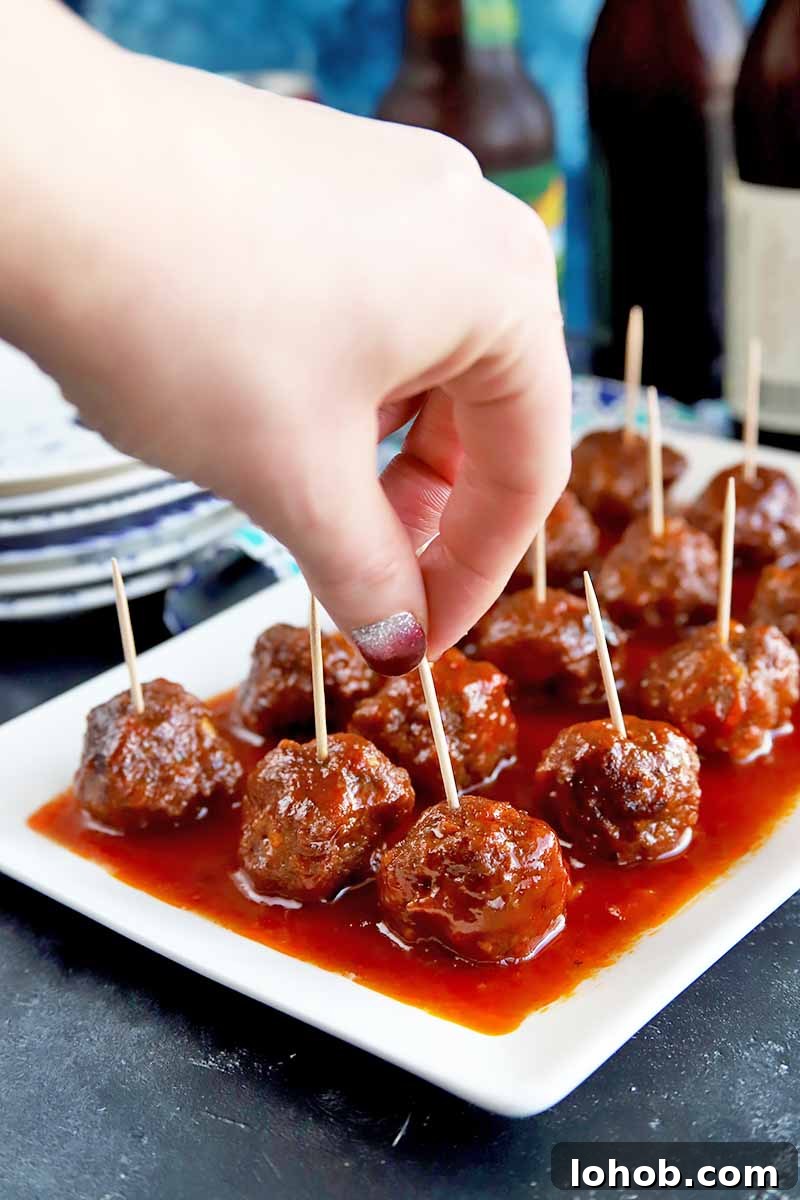 Sweet and Tangy Classic Meatballs Recipe for Weeknight Dinners 5 Horizontal image of a hand picking up a saucy appetizer with a toothpick inserted in it.