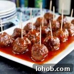 Horizontal image of a white platter with rows of meatballs covered in a red sauce with toothpicks inserted in them.