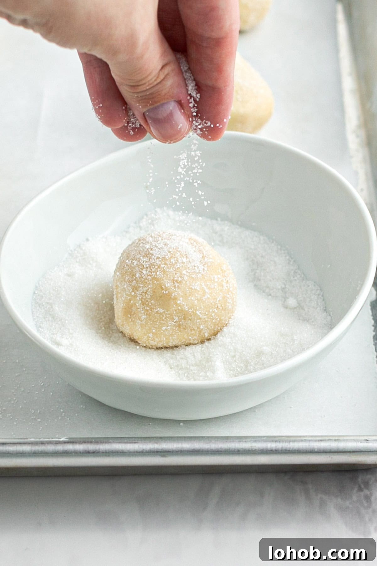 rolling a sugar cookie dough ball in granulated sugar