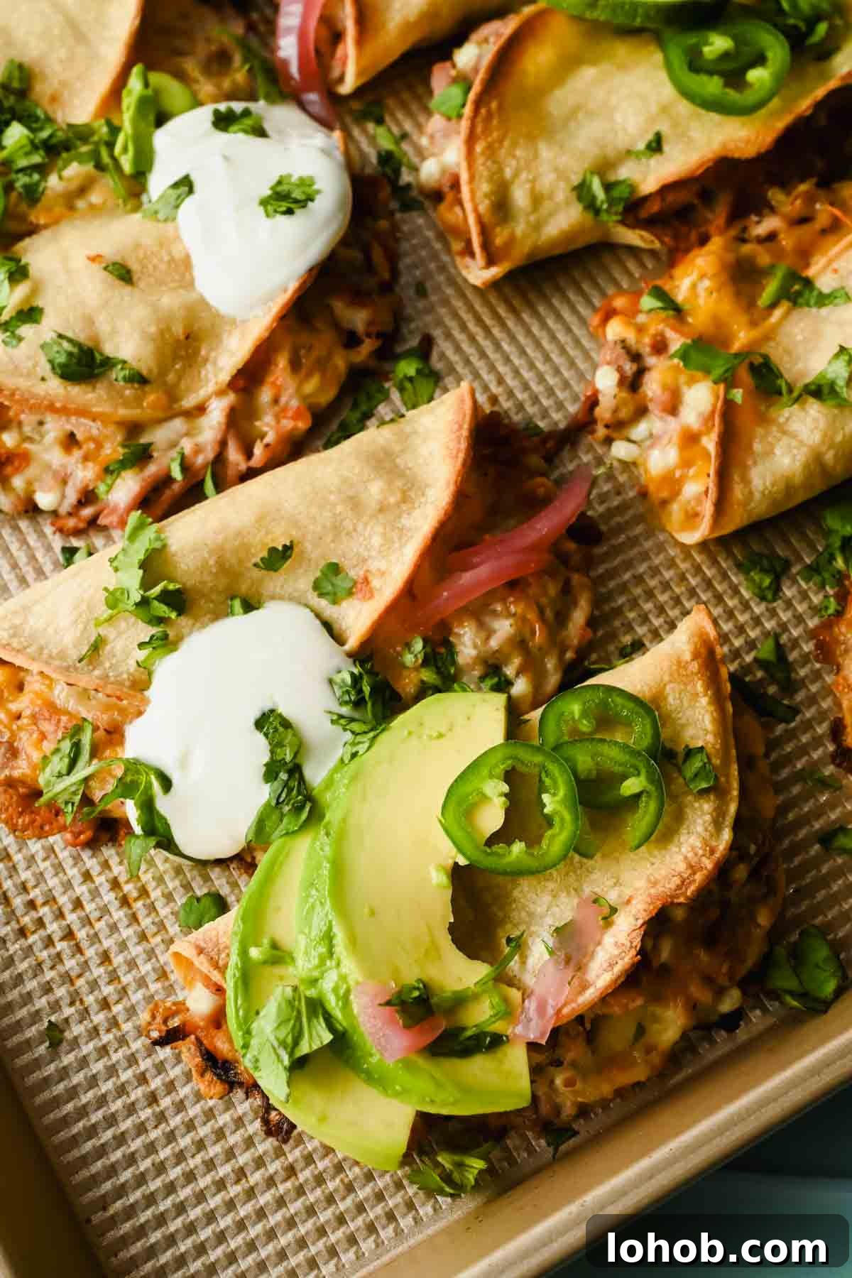 baked crispy pork tacos topped with herbs, lime wedges, avocado and sour cream.