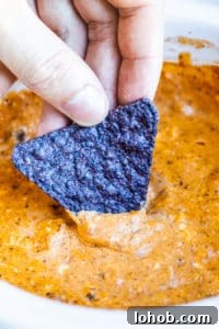 Crockpot Chili Cheese Dip Hand dipping blue tortilla chip into chili cheese dip.