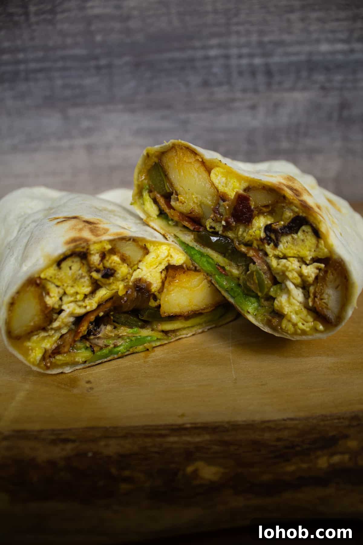Southwest Potato Breakfast Burrito Recipe with Salsa Verde 4 Southwest potato breakfast burrito cut in half showing potatoes, eggs, peppers and onions, bacon and cheese.