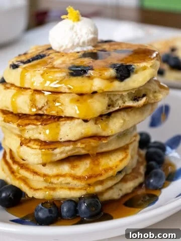 Lemon ricotta blueberry pancakes covered with syrup with a dollop of ricotta on top.