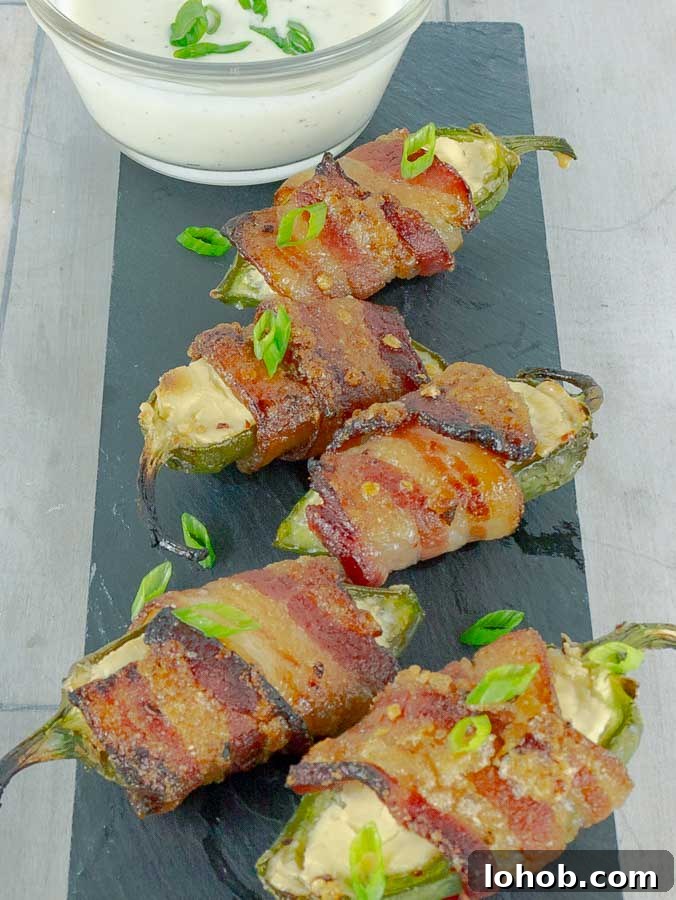 Bourbon-Candied Bacon Jalapeño Poppers Wrapped in Bacon 3 five Bourbon Candied Bacon Wrapped Jalapeno Poppers on a piece of slate with ranch