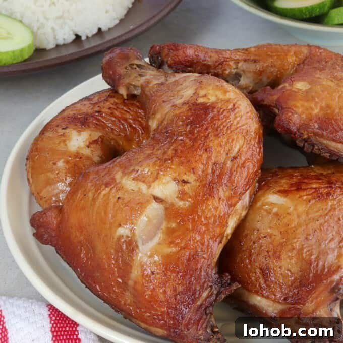 Crispy Soy-Glazed Chicken Recipe for Crunchy, Savory Skin 6 soy sauce chicken on a white platter with rice and sliced cucumbers and tomatoes on the side.