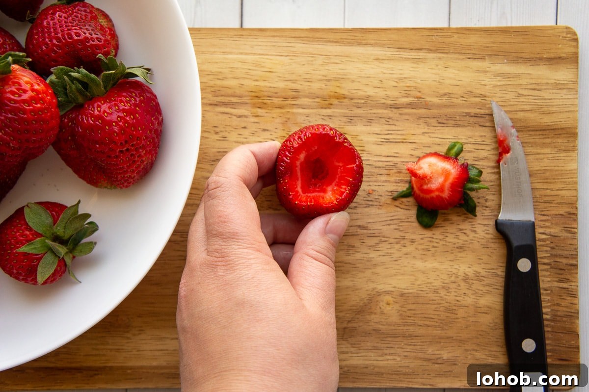 Homemade Strawberry Syrup: Simple Recipe for Fresh Fruit Topping 4 a bowl of berries beside a hand holding a freshly hulled strawberry, with the core and knife sitting beside it.