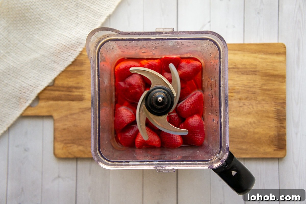 Homemade Strawberry Syrup: Simple Recipe for Fresh Fruit Topping 5 berries and water in a blender on a wooden cutting board.