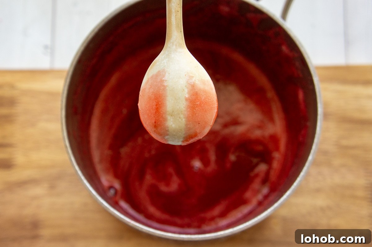 Homemade Strawberry Syrup: Simple Recipe for Fresh Fruit Topping 7 a beige spoon coated with strawberry syrup held over a pan.
