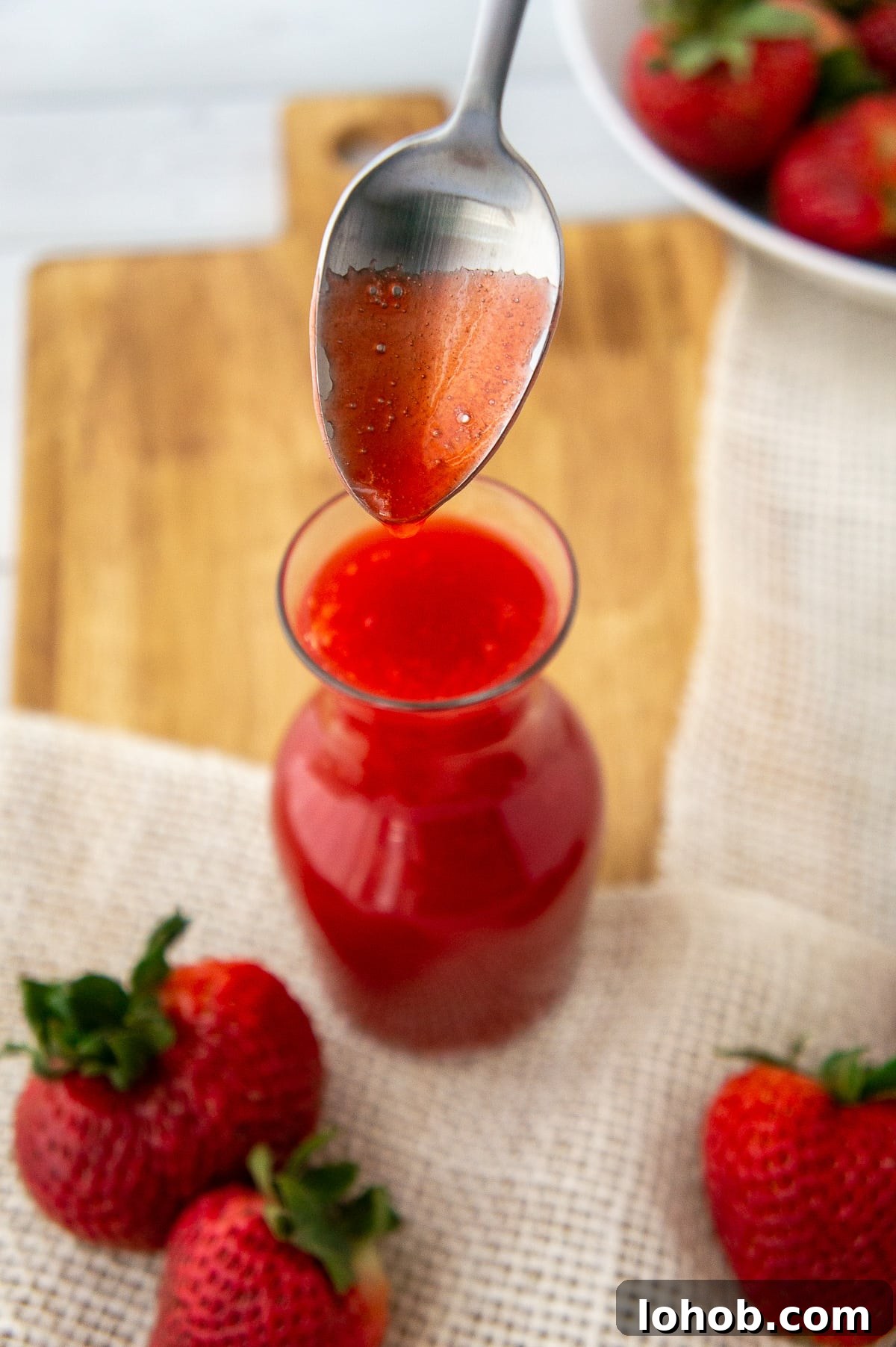 Homemade Strawberry Syrup: Simple Recipe for Fresh Fruit Topping 8 a spoon lifting strawberry sauce from a glass container.