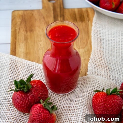 Homemade Strawberry Syrup: Simple Recipe for Fresh Fruit Topping 9 a glass carafe of strawberry syrup with fresh berries on a cutting board.