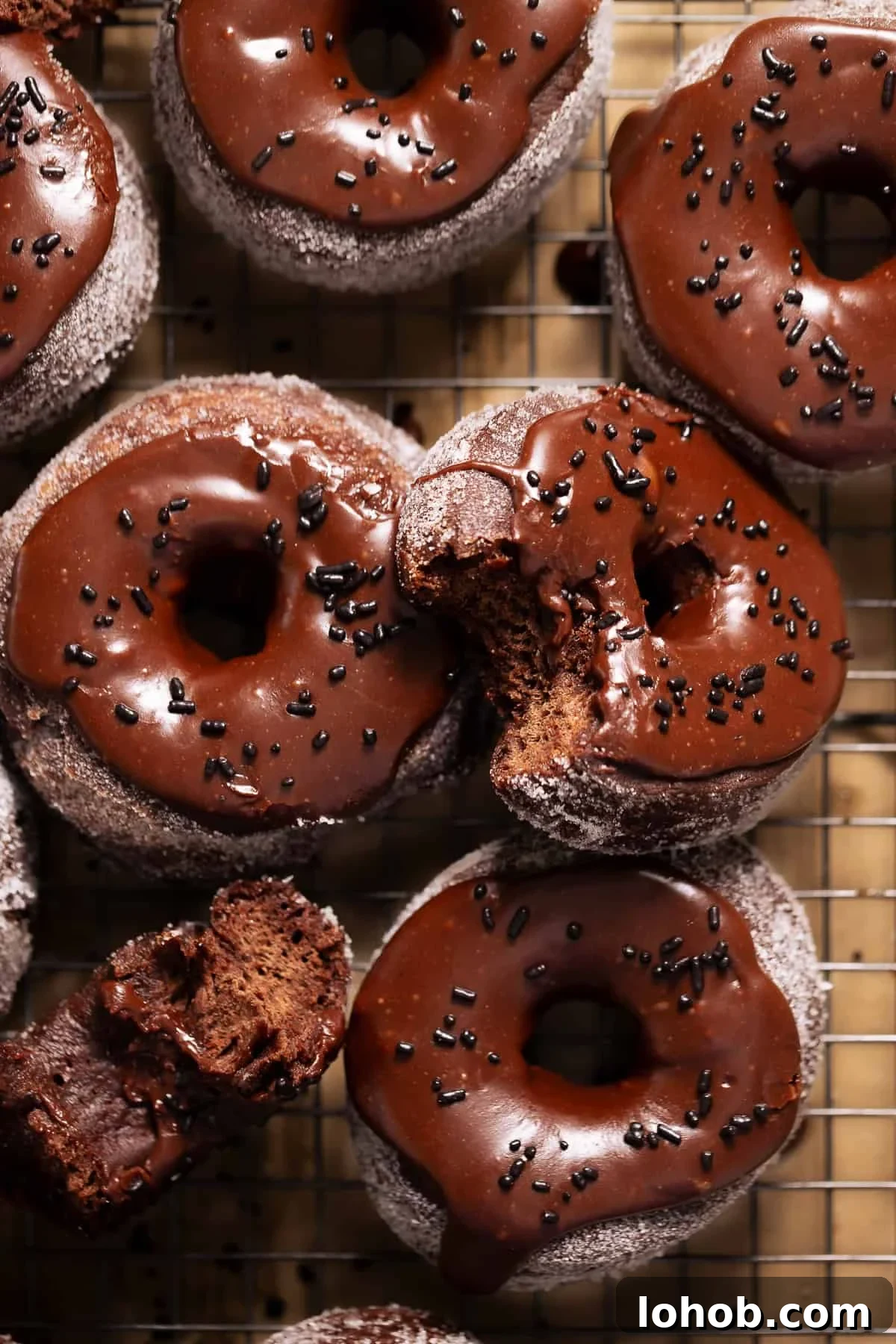 Chocolate frosted donuts with chocolate sprinkles on a wire baking rack.