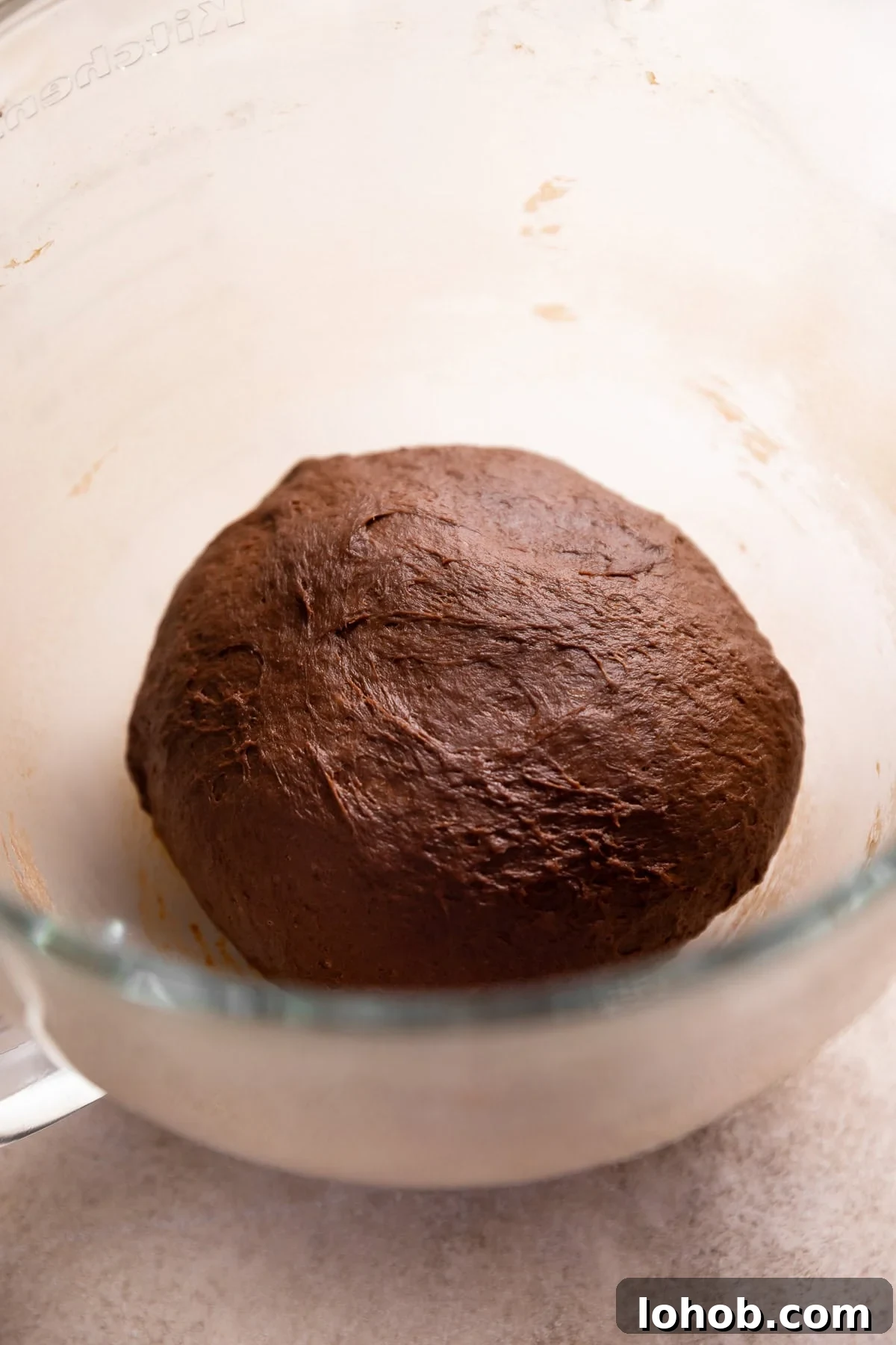 A ball of chocolate yeast dough resting in a glass bowl.