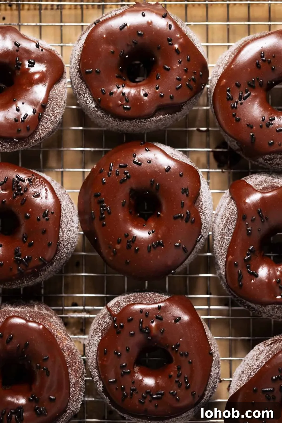 Chocolate donuts with chocolate frosting and chocolate sprinkles on a wire rack.