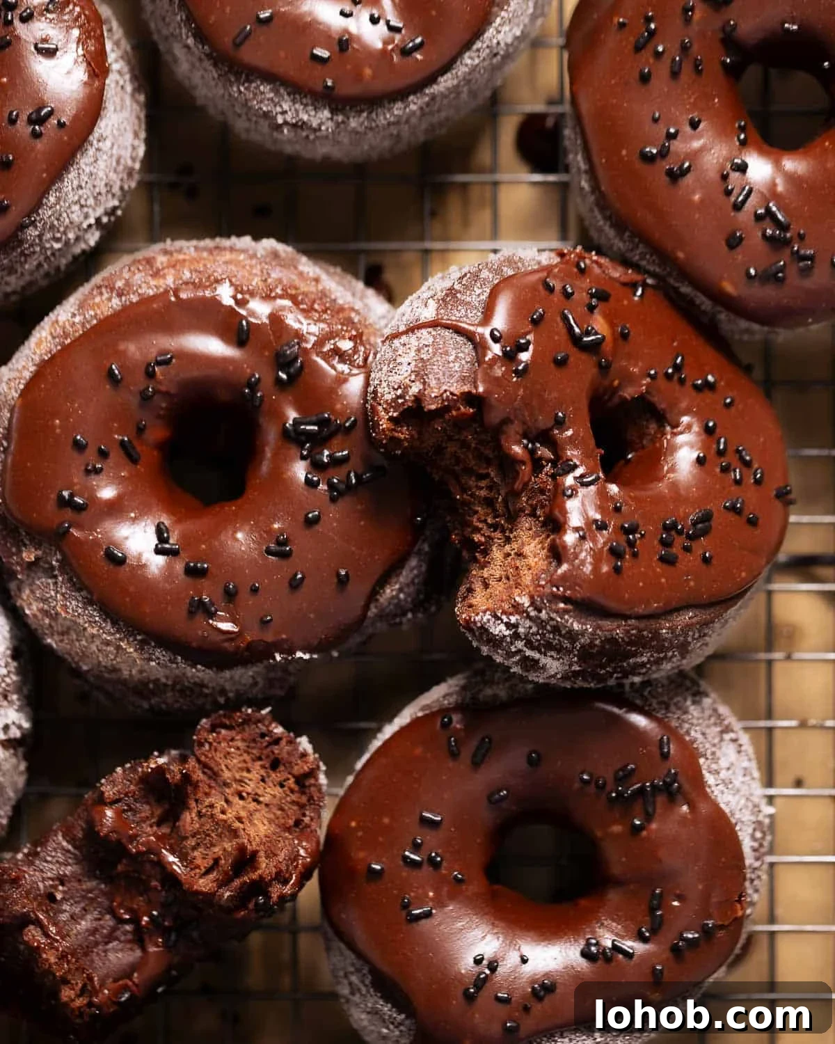 Double chocolate donuts with chocolate frosting and sprinkles on a wire rack.