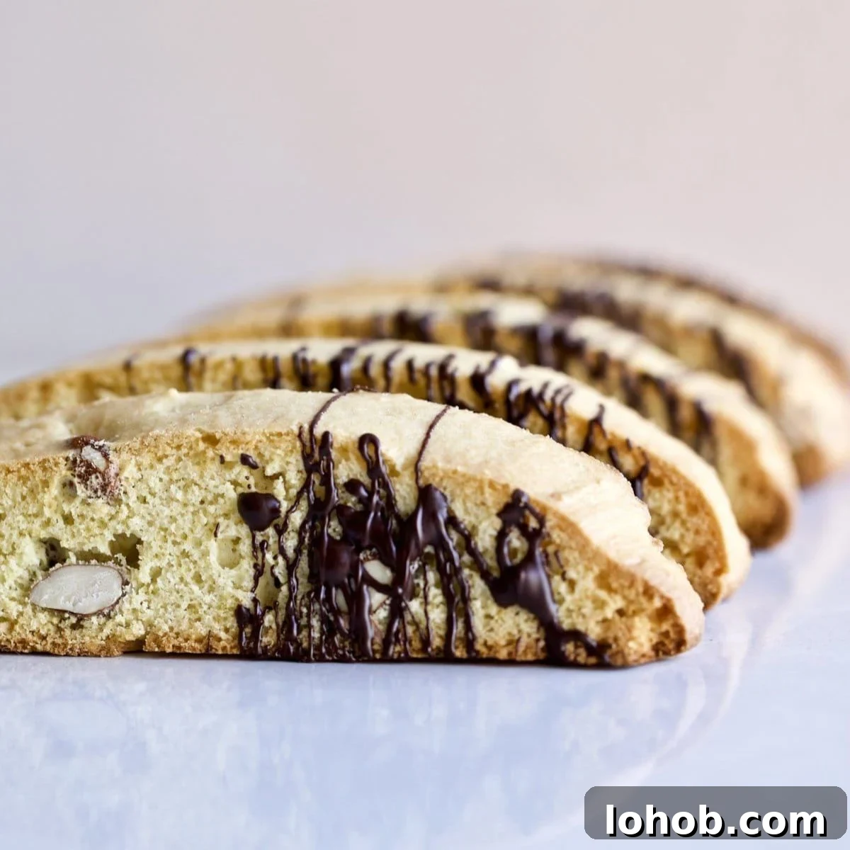 Italian almond biscotti on a white surface drizzled with chocolate.
