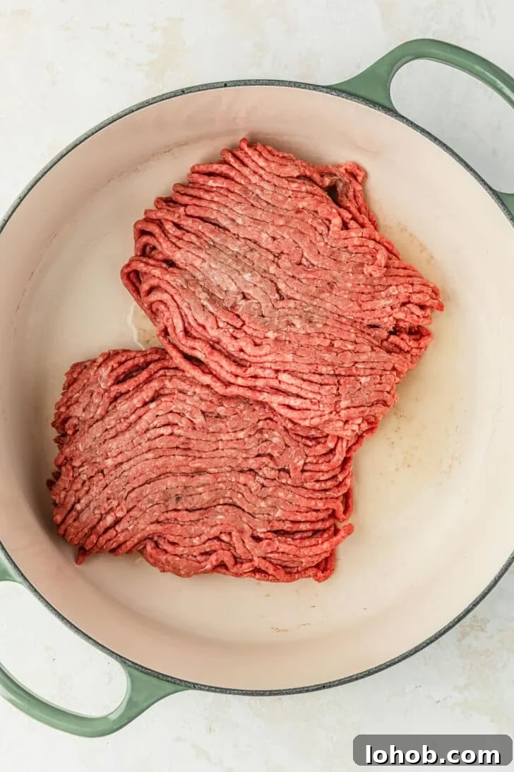 A green Dutch oven with raw ground beef.